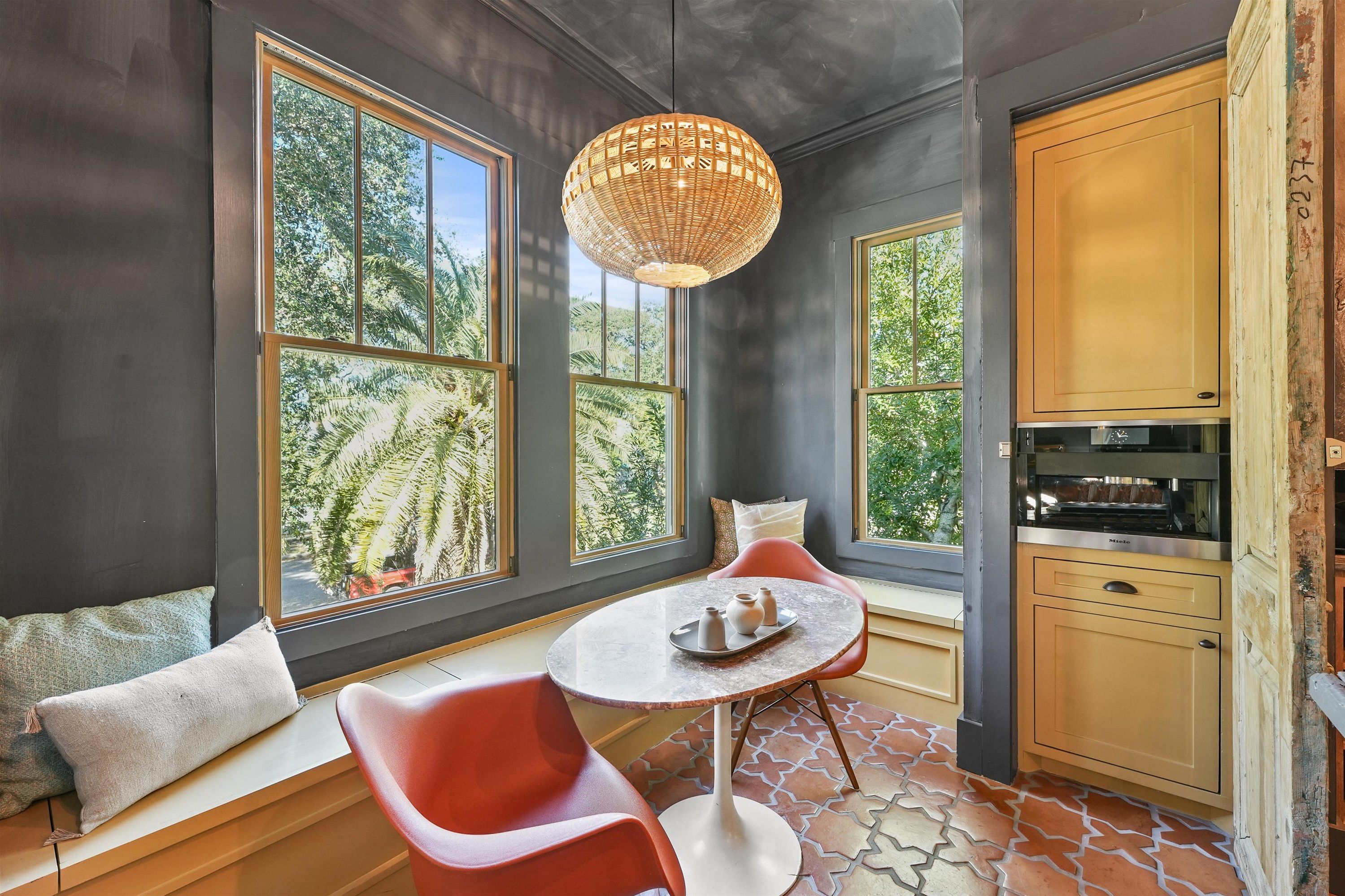 A modern kitchen with large windows, a dining area with red chairs, and a built-in stove.