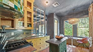 Une cuisine équipée d’une cuisinière à gaz, de meubles de rangement en bois, d’un garde-manger avec une porte en verre et d’un coin repas comprenant une table et des chaises.