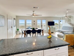 Una cocina amplia con encimera de granito, un comedor con vistas a la playa y una sala de estar con sofá y televisión.