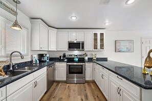A modern kitchen with white cabinets, a stainless steel oven, a microwave, and a granite countertop. - Our Infinity Pool by Ryson Vacation Rentals (Galveston)