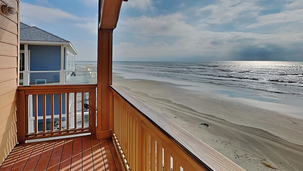 Un balcón de madera con vista a la playa y al océano.
