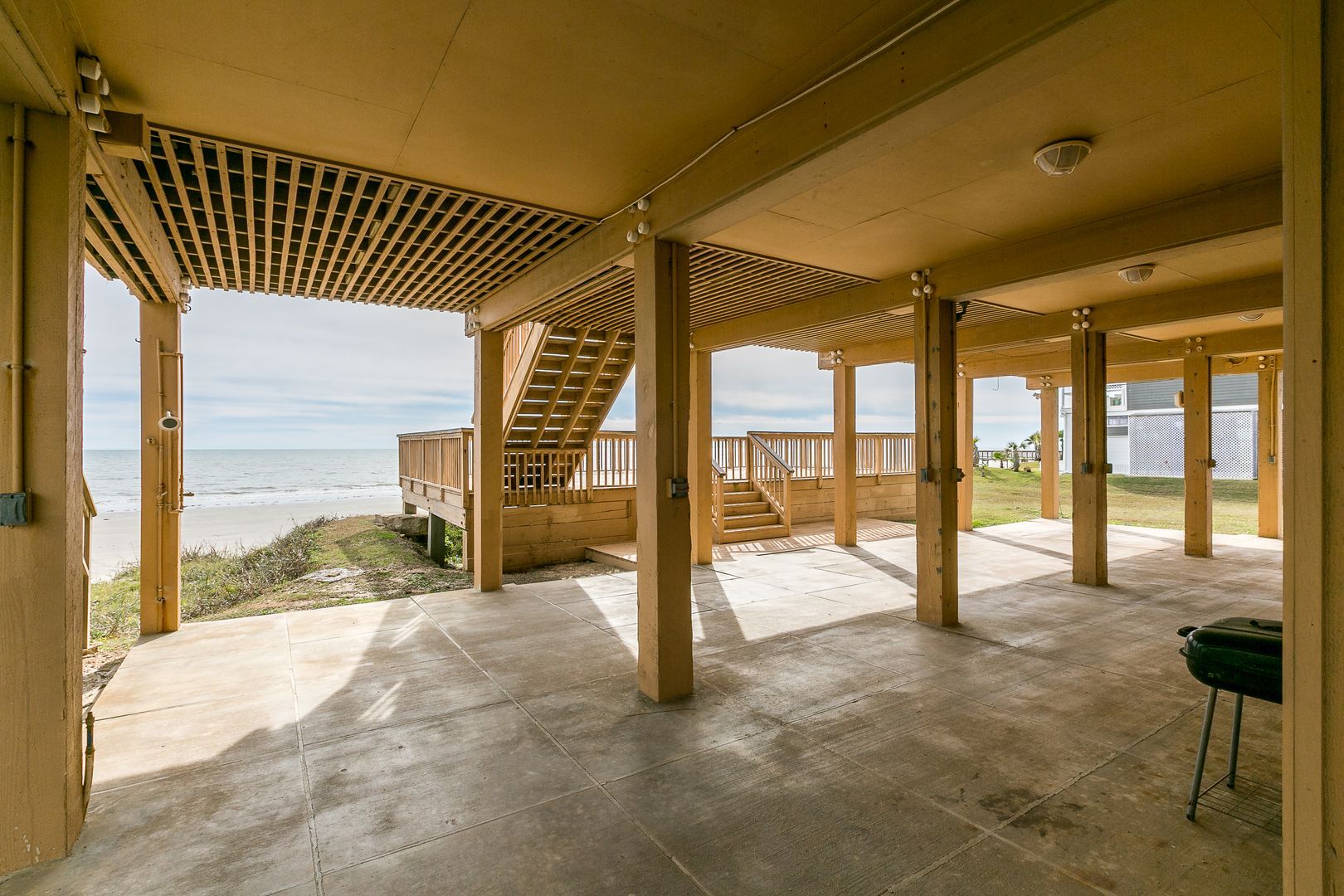 Een overdekt buitengebied met een houten terras en een trap naar uitzicht op het strand.