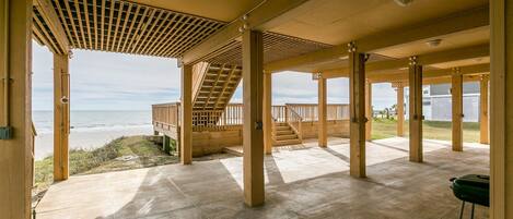 Een overdekt buitengebied met een houten terras en een trap naar uitzicht op het strand.