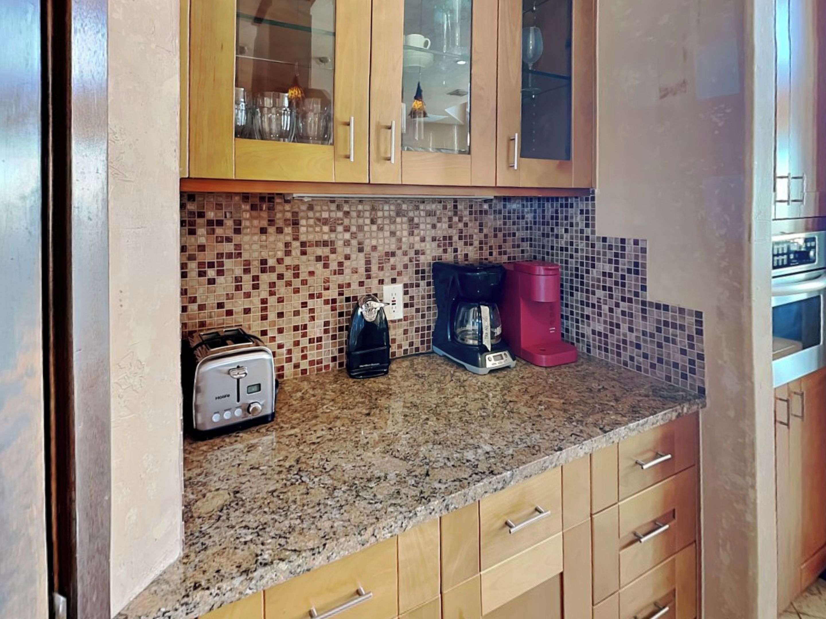 A kitchen with wooden cabinets, a tiled backsplash, a toaster, a coffee maker, and a microwave.