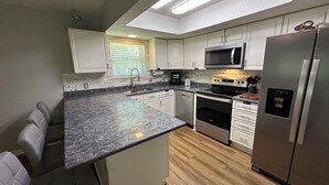 Uma cozinha moderna com armários brancos, geladeira de aço inoxidável, micro-ondas e forno embutido.