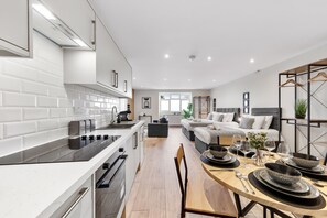 A modern kitchen with white cabinetry, a black countertop, and a dining area with a wooden table set for four.