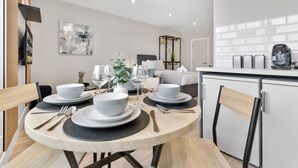 Un espace repas moderne avec une table ronde pour quatre personnes, un canapé et un coin cuisine équipé d’une machine à café.