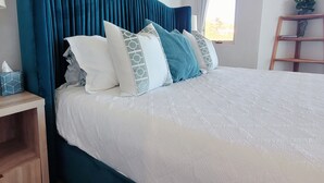 Una cama bien hecha con un cabecero color turquesa, ropa de cama blanca y almohadas estampadas.