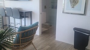 Una sala de estar moderna con televisor de pantalla plana, mobiliario de mimbre, una obra de arte enmarcada y un cesto de basura.