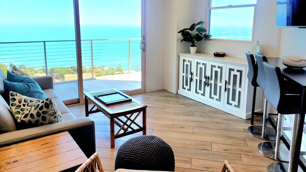 Un balcón amplio con vista al océano, un mueble blanco con puertas de vidrio y una zona de comedor con sillas y mesa.