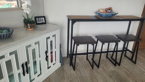 Una habitación con un armario blanco, un televisor montado en la pared y una pequeña mesa con taburetes.