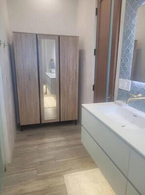 A modern bathroom with a wooden wardrobe, a white vanity, and a mirror with a decorative backsplash.