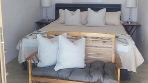 Un dormitorio con cama, mesitas de noche, un banco, una araña y un cuadro en la pared.