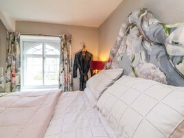 Un dormitorio con una cama grande, cortinas florales, una bata en un perchero y una ventana con vistas.