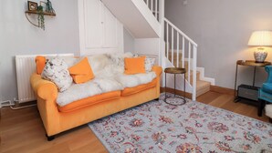 Un salon avec un canapé, un tapis à motifs, un escalier, une lampe et un radiateur.