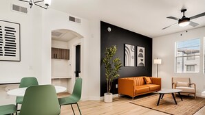 A modern living room with a black accent wall, a green sofa, a white coffee table, and a dining area with green chairs. - Boulevard Stays Chic 1BR Near Stadium Pool Access, Gym & Free Parking (Glendale)