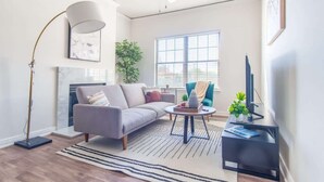 A modern living room with a grey sofa, a round coffee table, a floor lamp, a TV stand, and a fireplace.