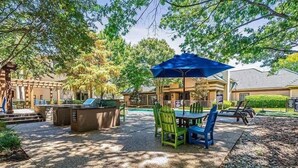 An outdoor patio area with a barbecue grill, a table with chairs, and a large umbrella. - Boulevard Stays Calm 1BR King Retreat Poolside Bliss Gym & Parking (Arlington)
