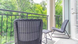 A balcony with wicker furniture and a view of lush greenery.