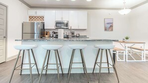 A modern kitchen with white cabinets, stainless steel appliances, and a bar area with stools.