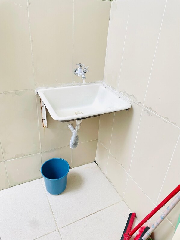A small bathroom with a white sink, a blue bucket, and cleaning tools.
