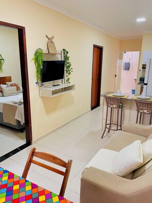 A living room with a TV, sofa, and a dining area with chairs and a table.