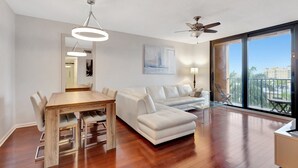 A modern living room with a wooden dining table, white sofa, and a ceiling fan. - Downtown 1BR Condo w/ Pool, Gym, Parking & Private Balcony (West Palm Beach)