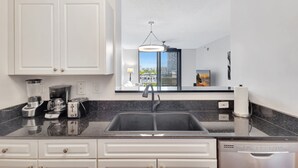 A modern kitchen with white cabinets, a black countertop, a built-in dishwasher, and a window with a city view. - Downtown 1BR Condo w/ Pool, Gym, Parking & Private Balcony (West Palm Beach)