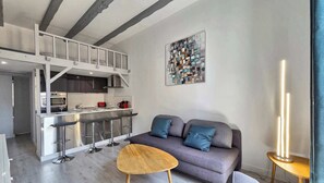 Una cocina moderna con entrepiso, un sofá gris con cojines azules y una mesa de centro de madera.