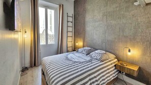 Un dormitorio con cama, ventana, escalera y dos luces fijadas a la pared.