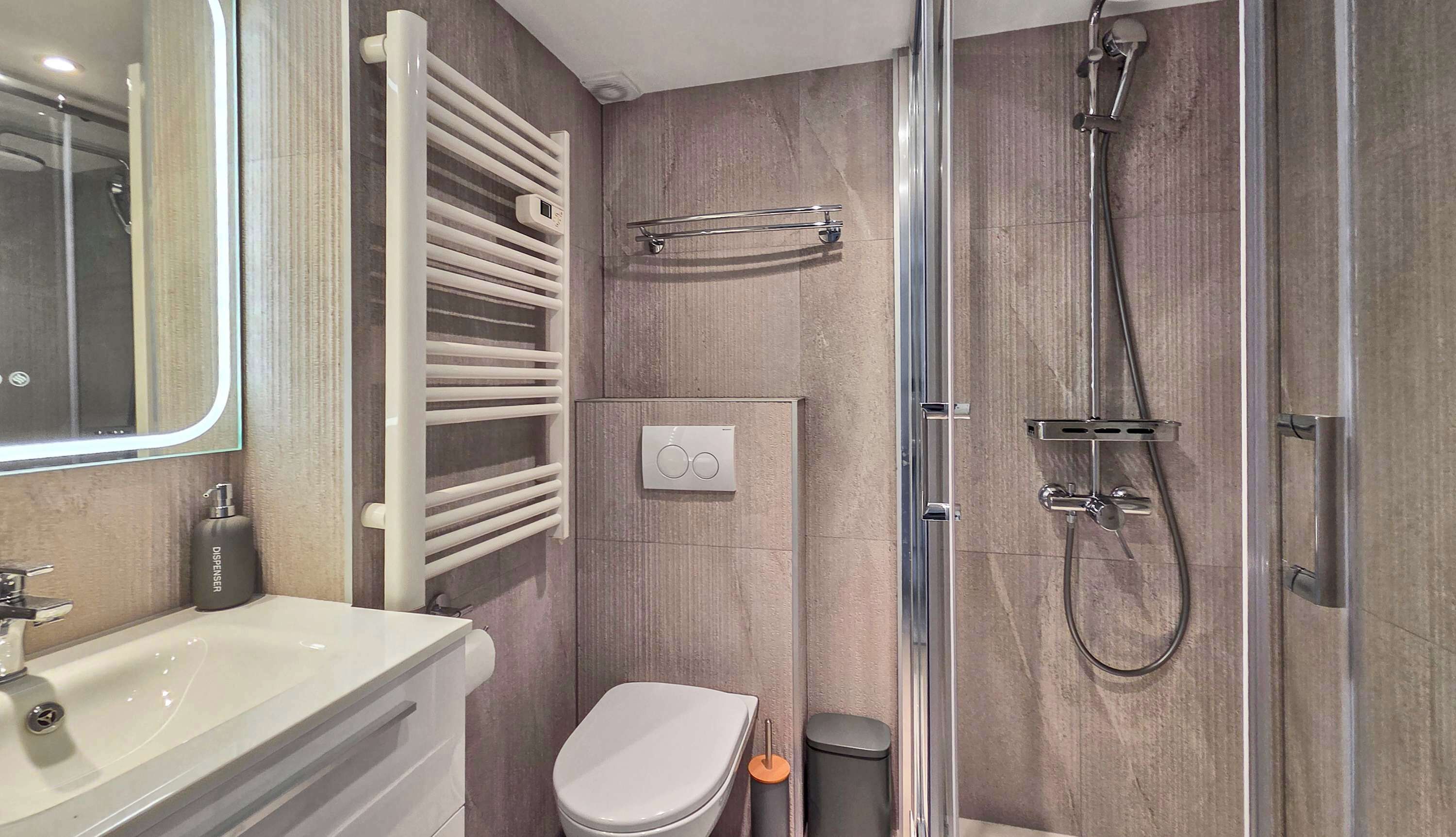 Un baño moderno con cabina de ducha de vidrio, inodoro blanco, toallero y lavamanos con espejo.