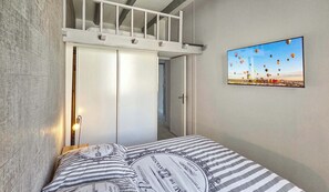 Un dormitorio con cama, un cuadro de globos aerostáticos y un altillo sobre la cama.