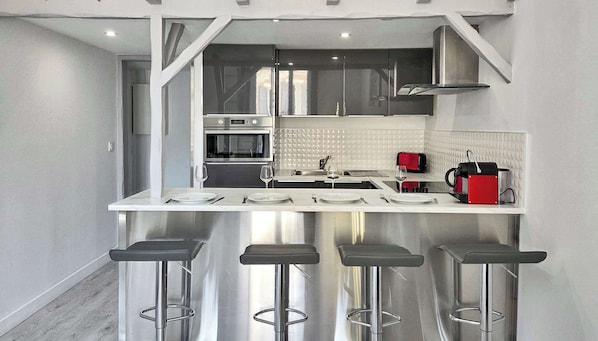 Una cocina moderna con electrodomésticos de acero inoxidable, una encimera blanca y tres taburetes de bar.