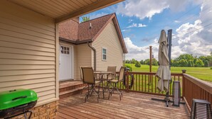 Une terrasse couverte avec une table et des chaises, un barbecue et une vue sur un champ verdoyant.