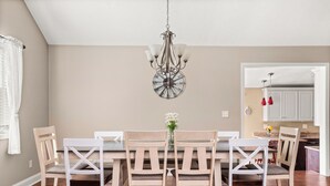 Un coin repas avec une table et des chaises en bois, un lustre et une cuisine en arrière-plan.