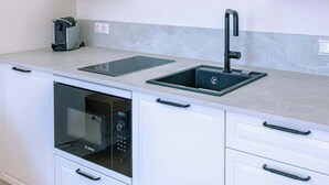 Una cocina moderna con armarios blancos, horno empotrado, pileta y cafetera.