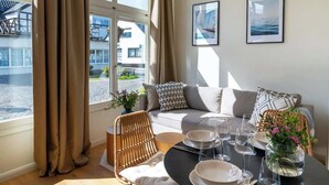 Una sala de estar moderna con un sofá, una mesa de comedor preparada para cuatro personas y un gran ventanal con cortinas.