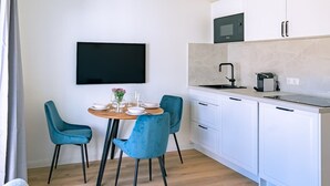 A modern kitchen with white cabinets, a black microwave, and a round dining table with blue chairs. - 2-Raum Appartement „Nr. 3“ mit großer Terrasse (Rostock)