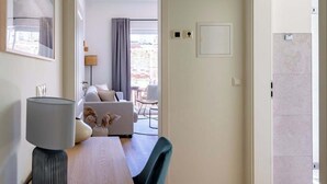 A modern living room with a sofa, a dining table with a lamp, and a view of the outside. - 2-Raum Appartement „Nr. 3“ mit großer Terrasse (Rostock)