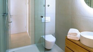 Un baño moderno con cabina de ducha de vidrio, inodoro blanco y tocador de madera con lavamanos redondo.
