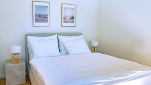 Un lit bien fait, avec du linge de lit blanc, deux tables de chevet avec des lampes et deux tableaux encadrés accrochés au mur.