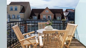 Un balcon avec des chaises et une table en bois, un vase de fleurs et une vue sur les maisons voisines.