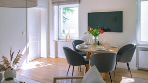 Un coin repas avec une table ronde dressée pour quatre personnes, entourée de chaises grises. Un vase rempli de fleurs est posé sur la table, et une grande fenêtre offre une vue sur la verdure à l’extérieur.