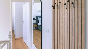 Ein Flur mit Holzboden, weißen Wänden und einem Spiegel, der ein Bett und eine Lampe reflektiert.