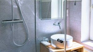 Ein modernes Badezimmer mit Duschkabine aus Glas, einem großen Spiegel und einem Holzwaschtisch mit Waschbecken und Handtuchhalter.