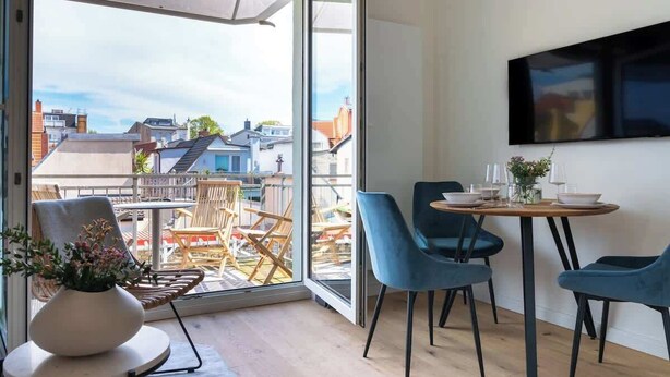 Ein moderner Essbereich mit großem Fenster, einem runden Tisch und blauen Stühlen.