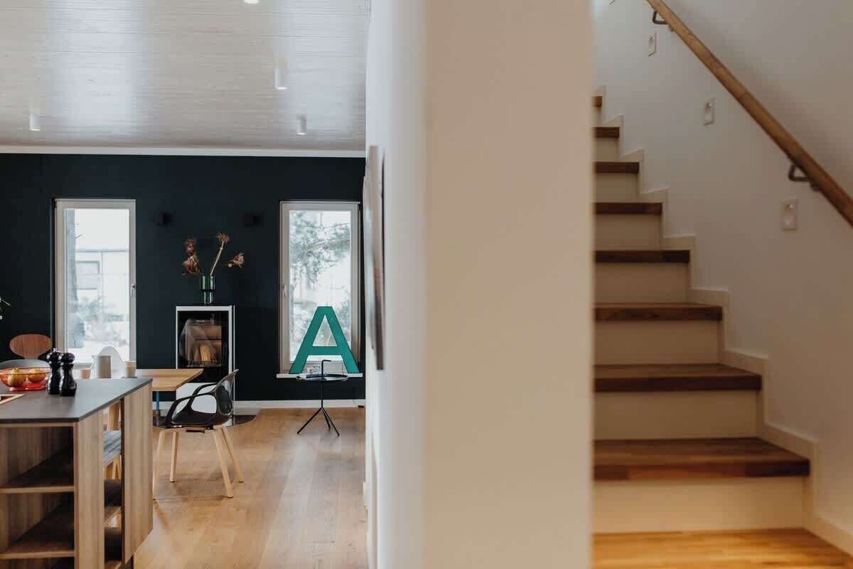 A modern interior with a staircase, a dining area with a table and chairs, and a large 'A' decoration on the wall.