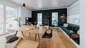 A modern living room with a wooden dining table, black chairs, a green sofa, and a large window with a view of trees. - Aloha Pruchten (Pruchten)