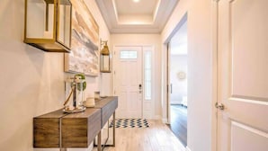 A hallway with a wooden console table, a wall-mounted mirror, and a door at the end. - Go 10 - 15530 WG in Winter Garden (Winter Garden)
