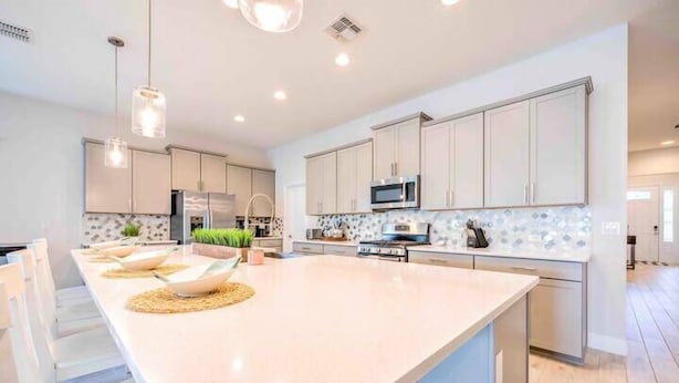 A modern kitchen with a large island, stainless steel appliances, and light-colored cabinetry. - Go 10 - 15530 WG in Winter Garden (Winter Garden)